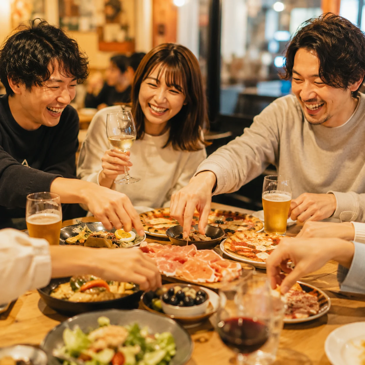 友人3人がイタリアン料理とお酒を楽しみながら笑い合う集まり
